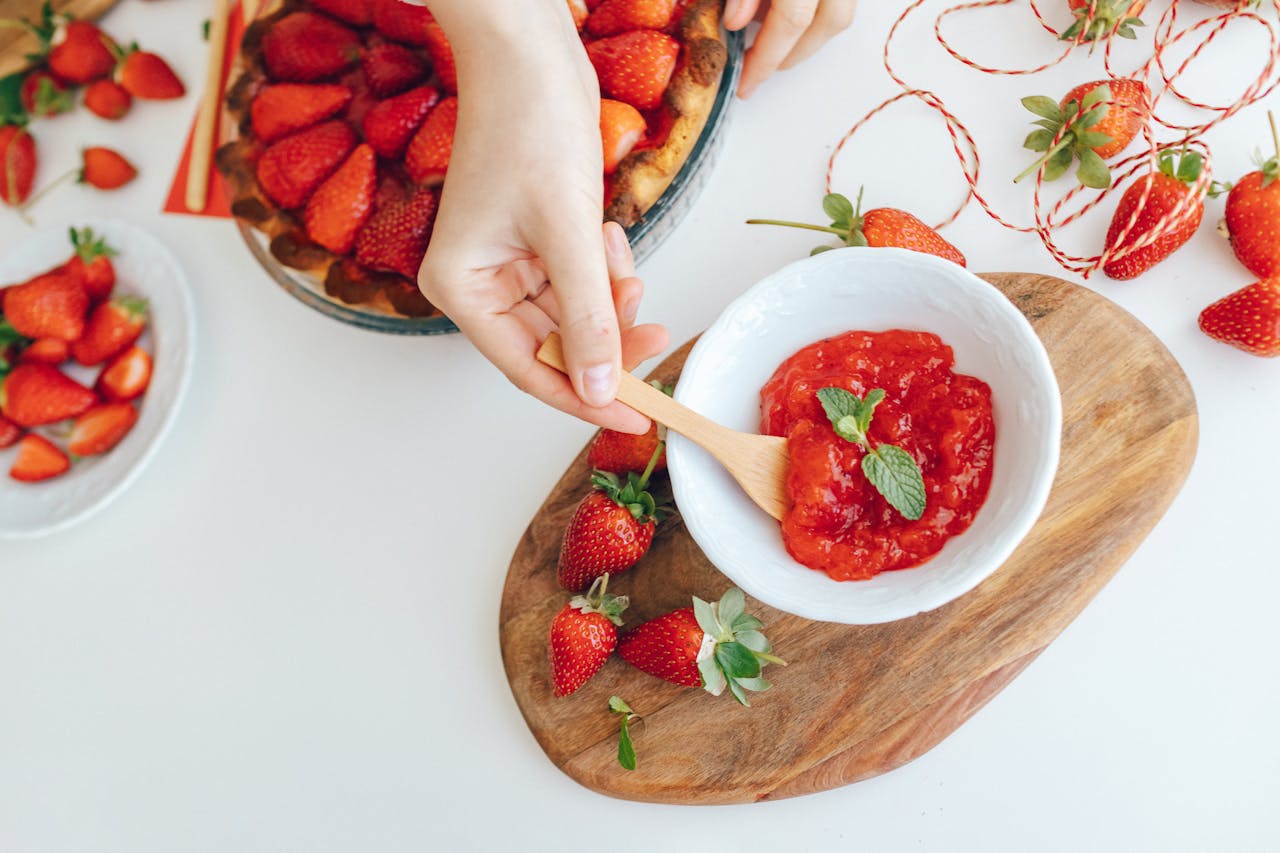 about-01 Close-up of hands making fresh strawberry jam with mint garnish.